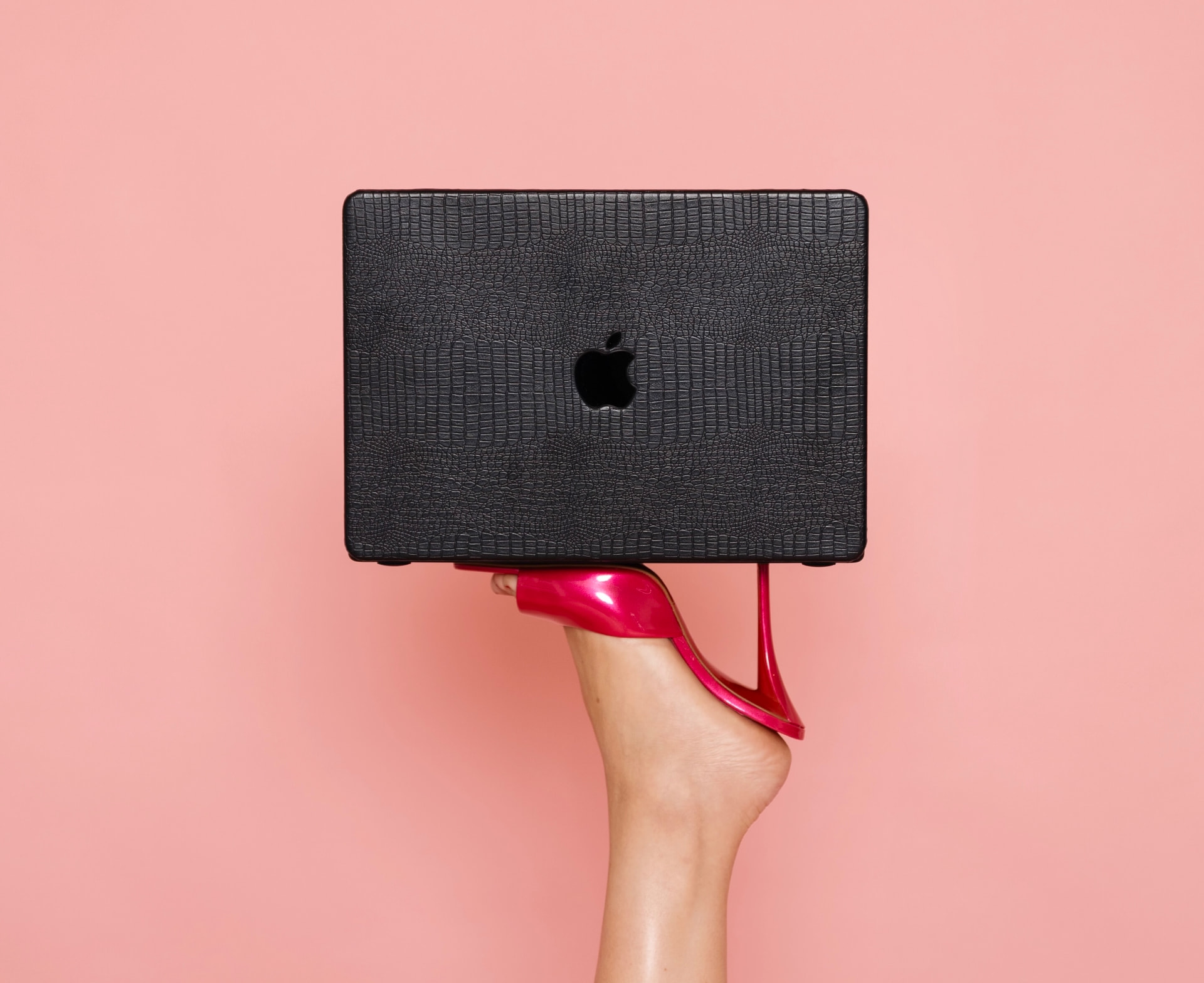 Pink heel balancing a black laptop against a pink backdrop